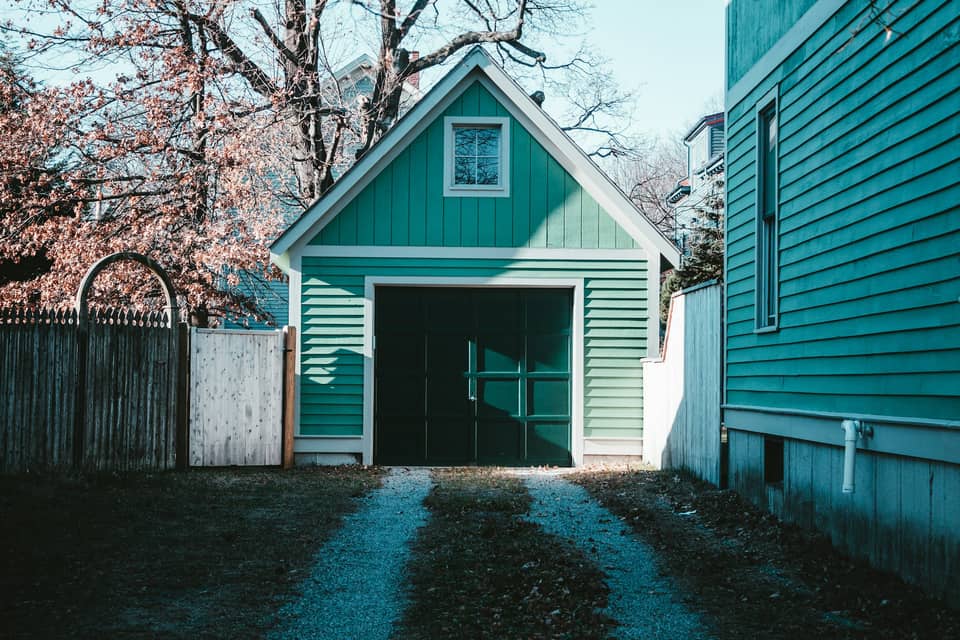 A small green carriage-house garage at the end of a gravel driveway