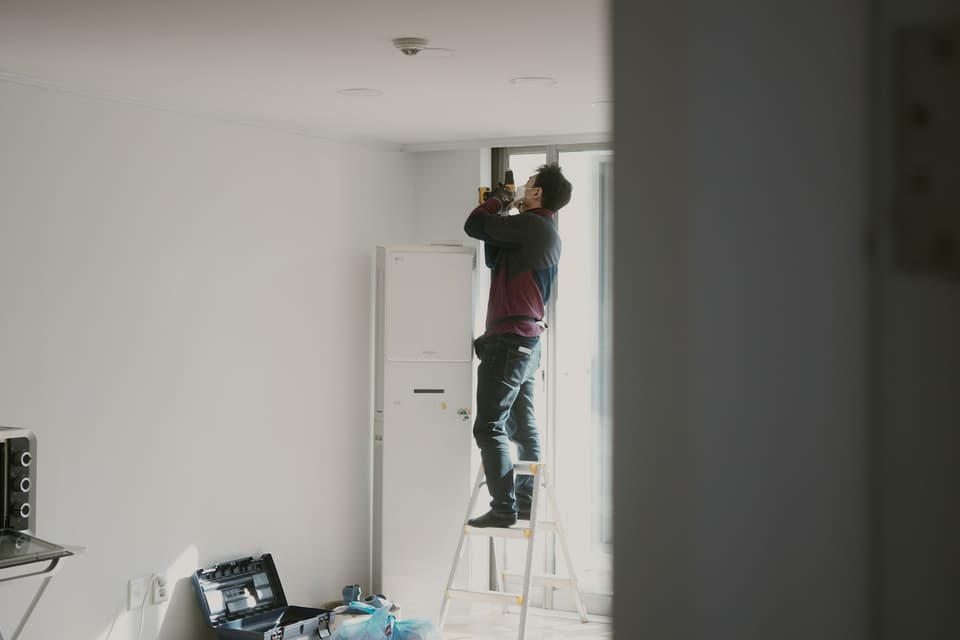 A worker on a stepladder fitting something above a doorway in an empty room